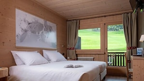 Una habitació de fusta amb un llit, un quadre abstracte gran, una vista d'un paisatge verd a través d'una finestra i un escriptori de fusta.