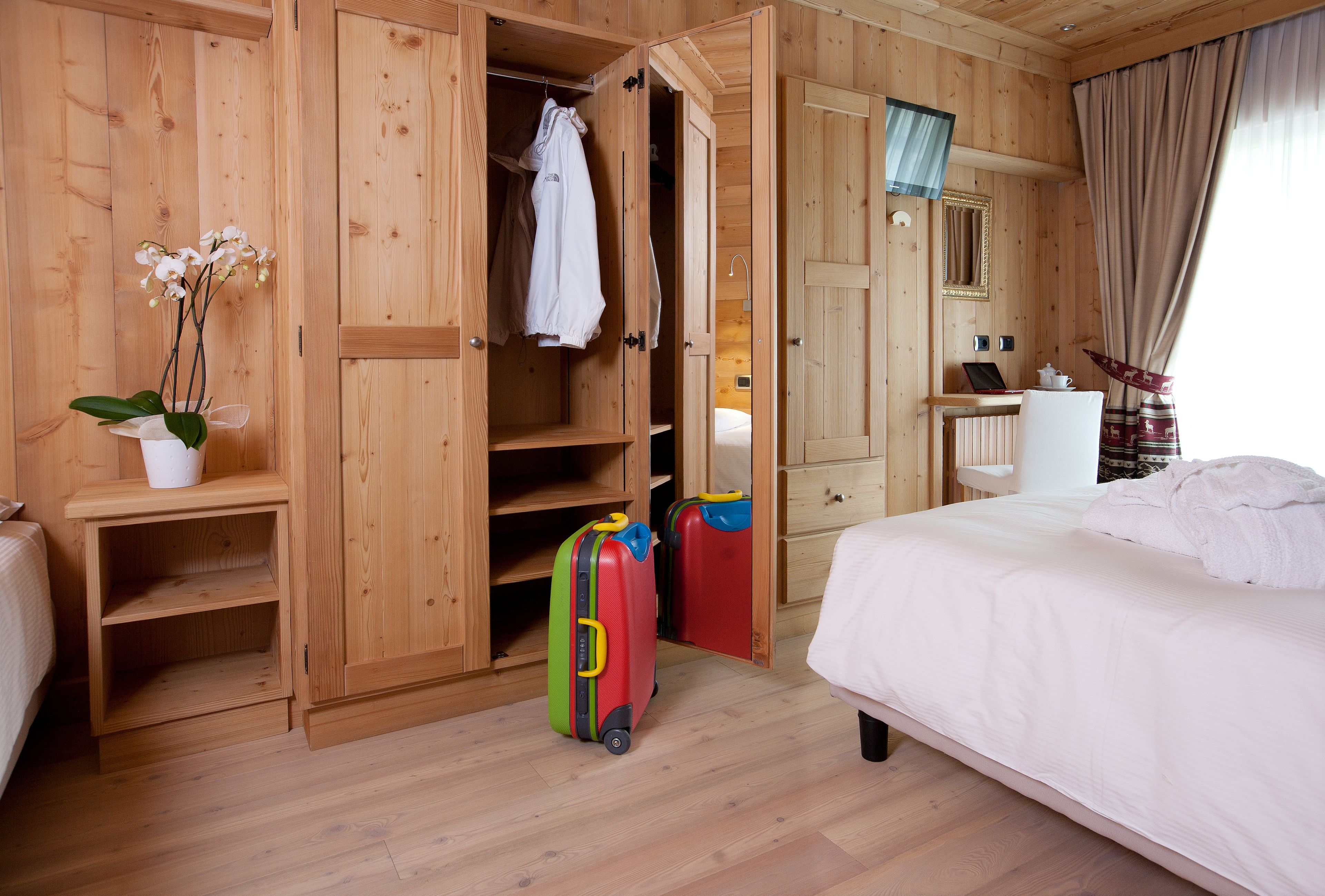 A wooden room with a bed, a wardrobe, a desk, and two suitcases.