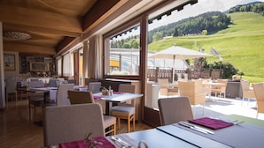 Restaurant amb vista a un vessant verd, interior de fusta i terrassa.