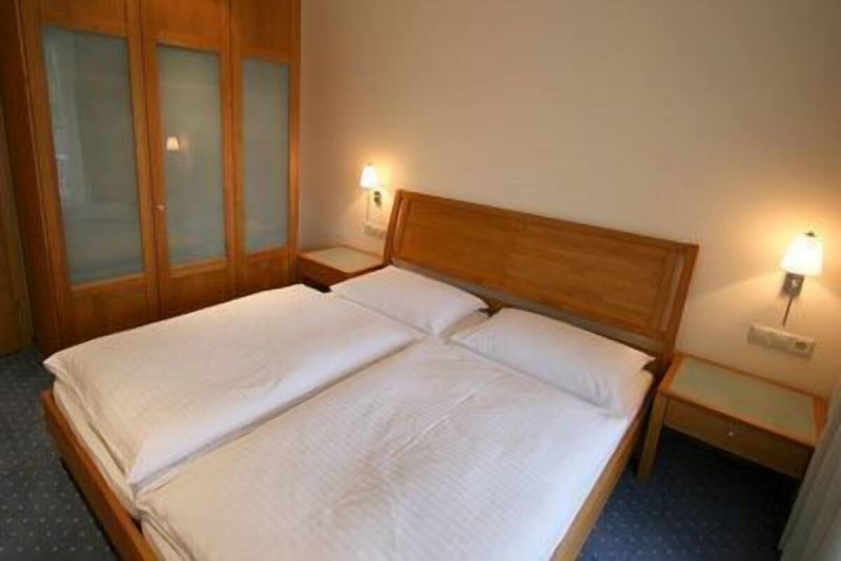 A double bed with wooden headboard and nightstands, a wooden wardrobe with frosted glass doors, and wall-mounted lamps.