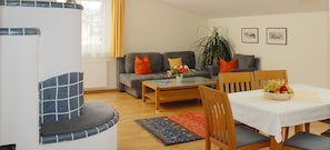 A living room with a sofa, a coffee table, a dining table with chairs, a plant, and framed pictures on the wall. - Appartements Tritscher (Schladming)