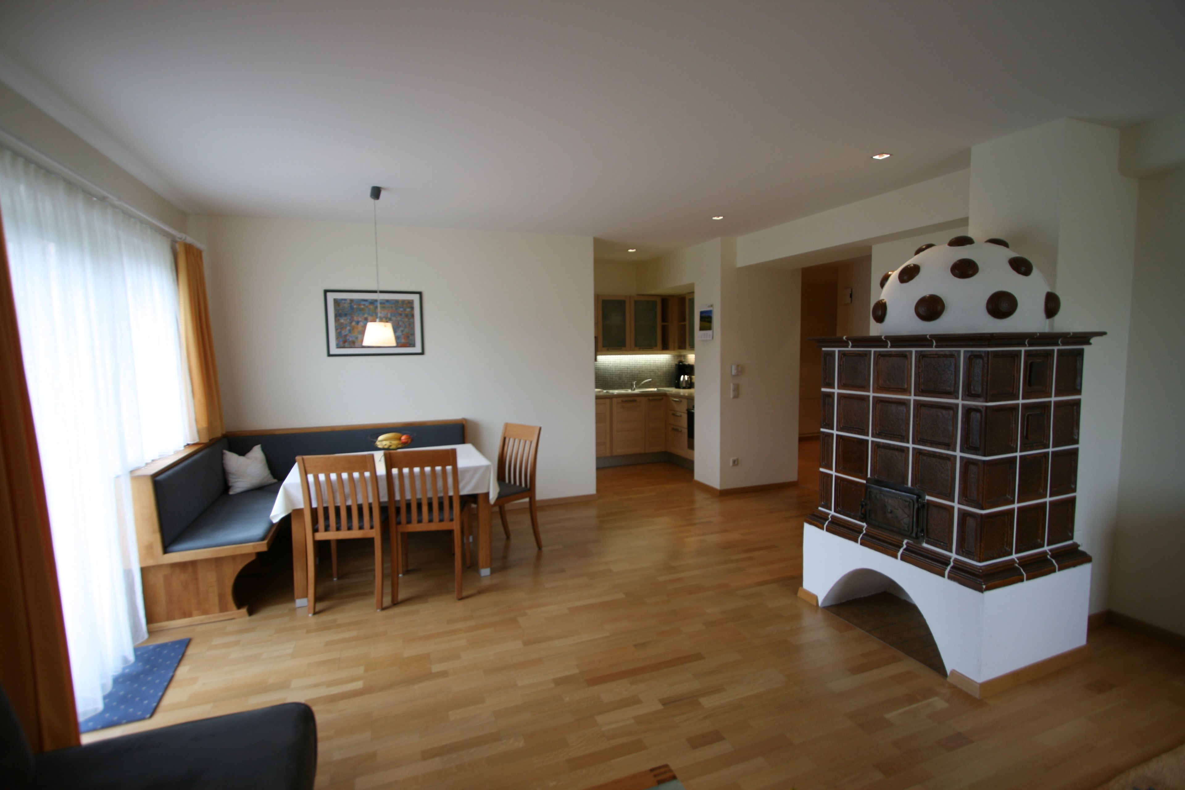 A modern living room with a wooden floor, a dining area with a table and chairs, a built-in fireplace, and a kitchen in the background.