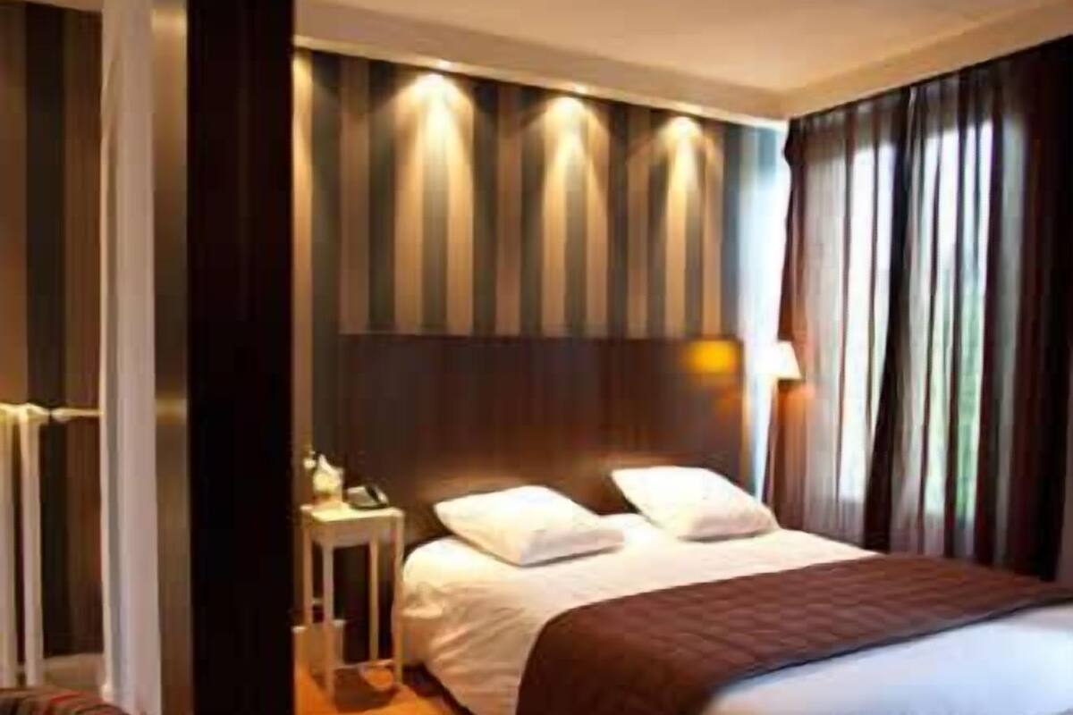 A hotel room with a bed, a bedside table, a chair, and a lamp.