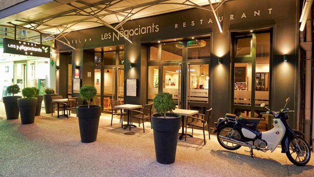 An outdoor seating area with tables and chairs, a motorcycle, and potted plants. - Hôtel Les Negociants (Valence)