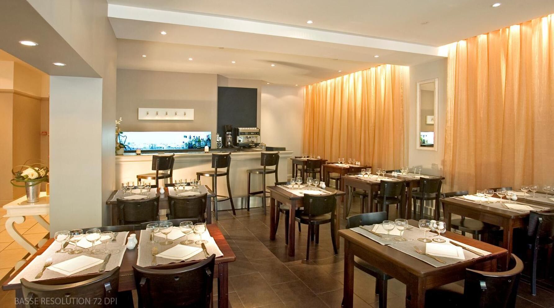 Un restaurante con varias mesas preparadas para el servicio, una zona de bar y vistas a la ciudad.