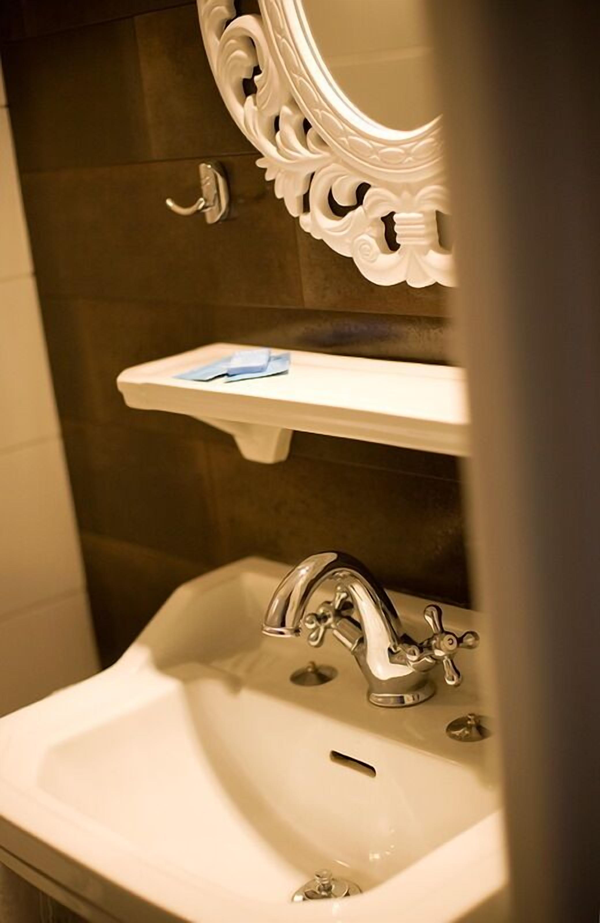 Une salle de bain avec un lavabo blanc, un miroir aux motifs décoratifs et un porte-serviettes.