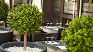 An outdoor dining area with tables and chairs, potted plants, and a building with signage reading "Les Négociants." - Hôtel Les Negociants (Valence)