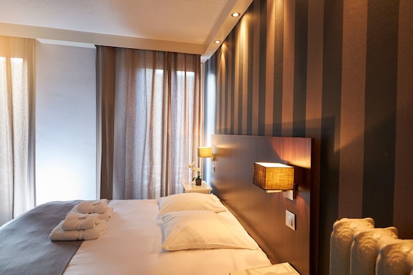Una habitación de hotel con una cama grande, una mesita de noche con lámpara y vistas al exterior por la ventana.