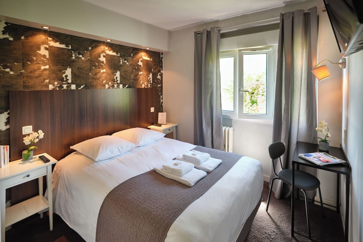A hotel room with a large bed, a desk, a chair, a window with curtains, and a wall with a textured design.