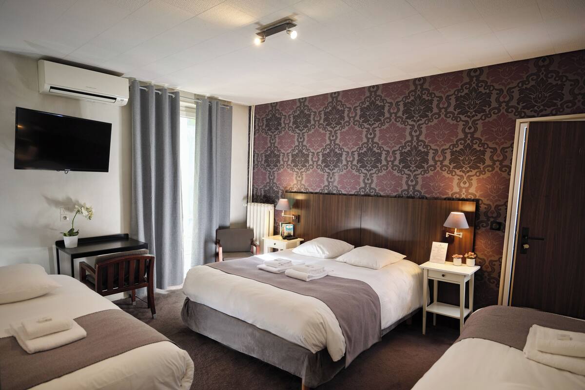 A hotel room with a large bed, two smaller beds, a desk, a TV, and a patterned wall.