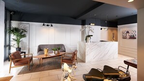 A modern hotel lobby with a marble reception desk, leather seating, a coffee table, and a large potted plant. - Hôtel Les Negociants (Valence)