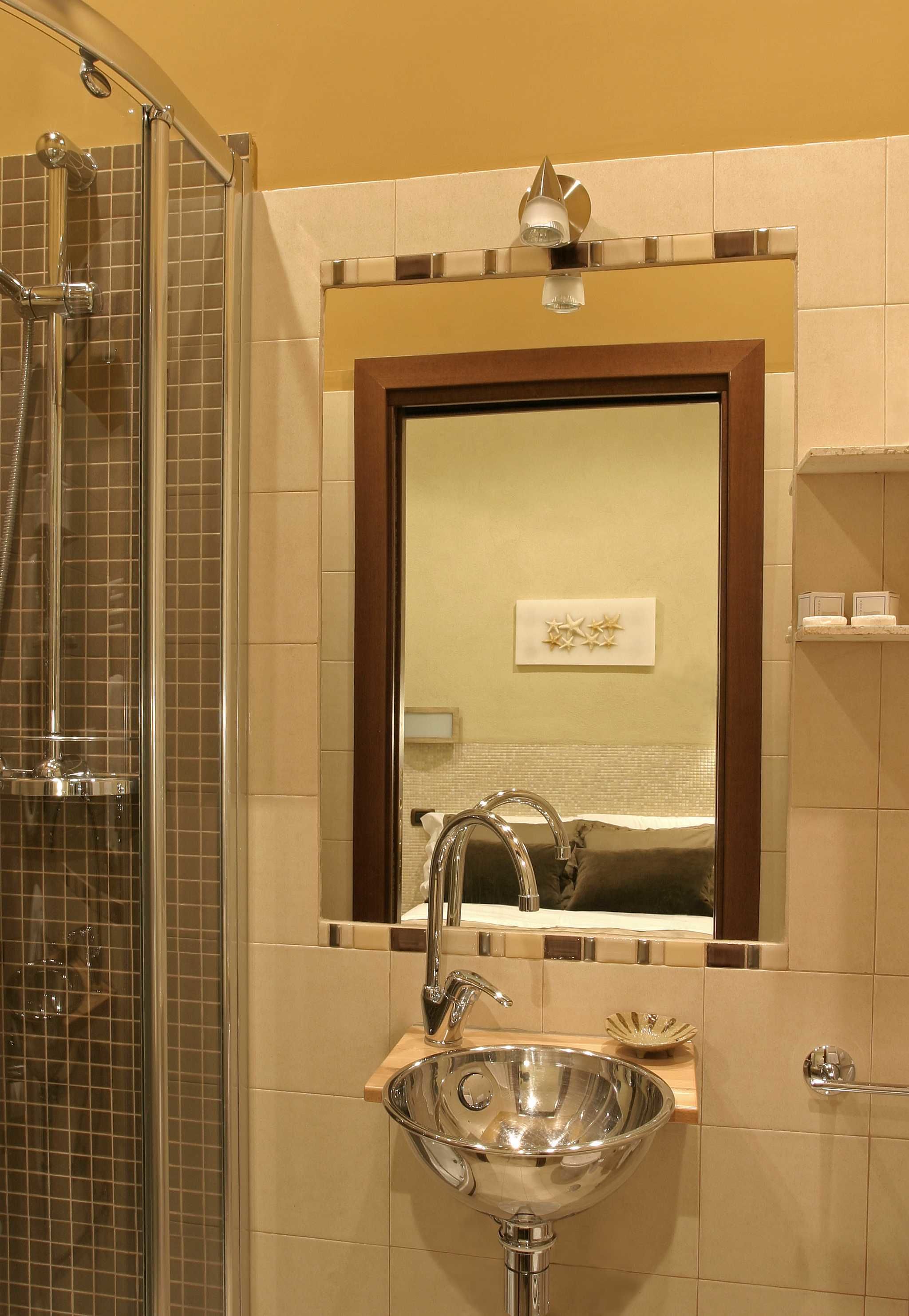 A bathroom with a glass-enclosed shower, a sink with a mirror above it, and a wall-mounted shelf with toiletries.
