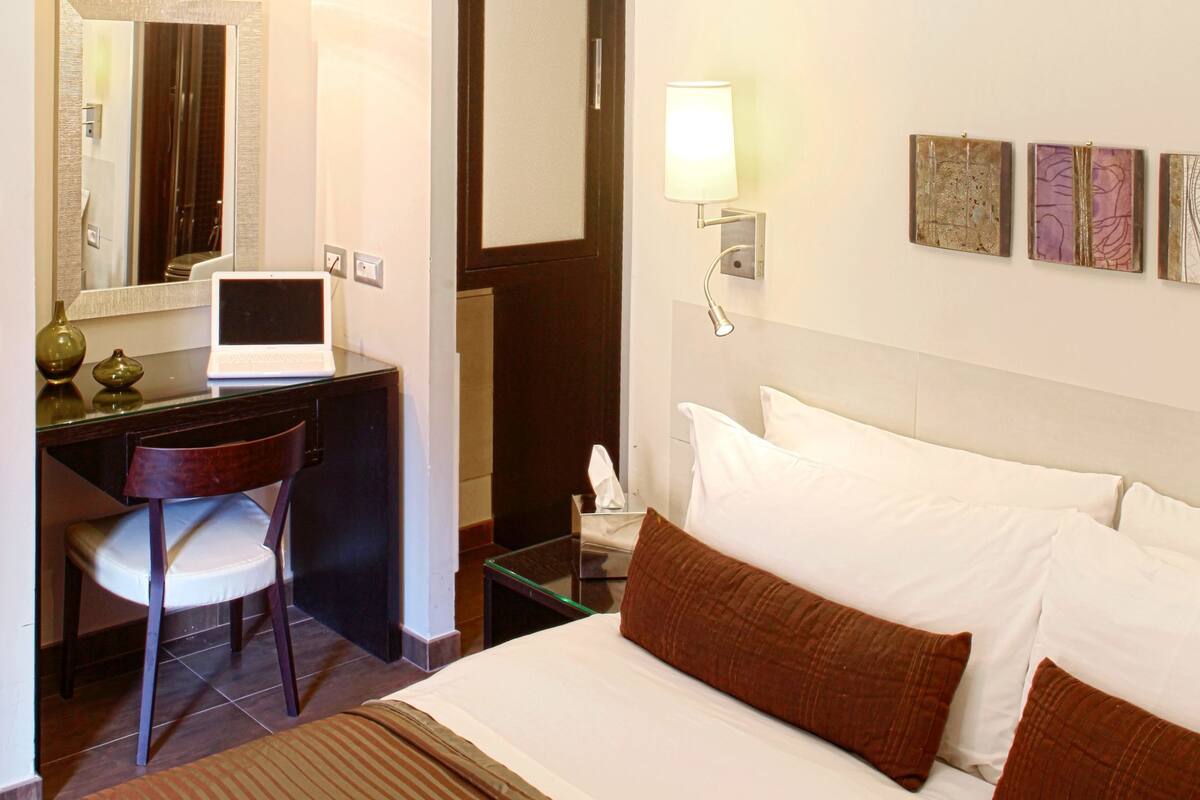 Habitación de hotel con cama, escritorio, silla y un espejo grande.