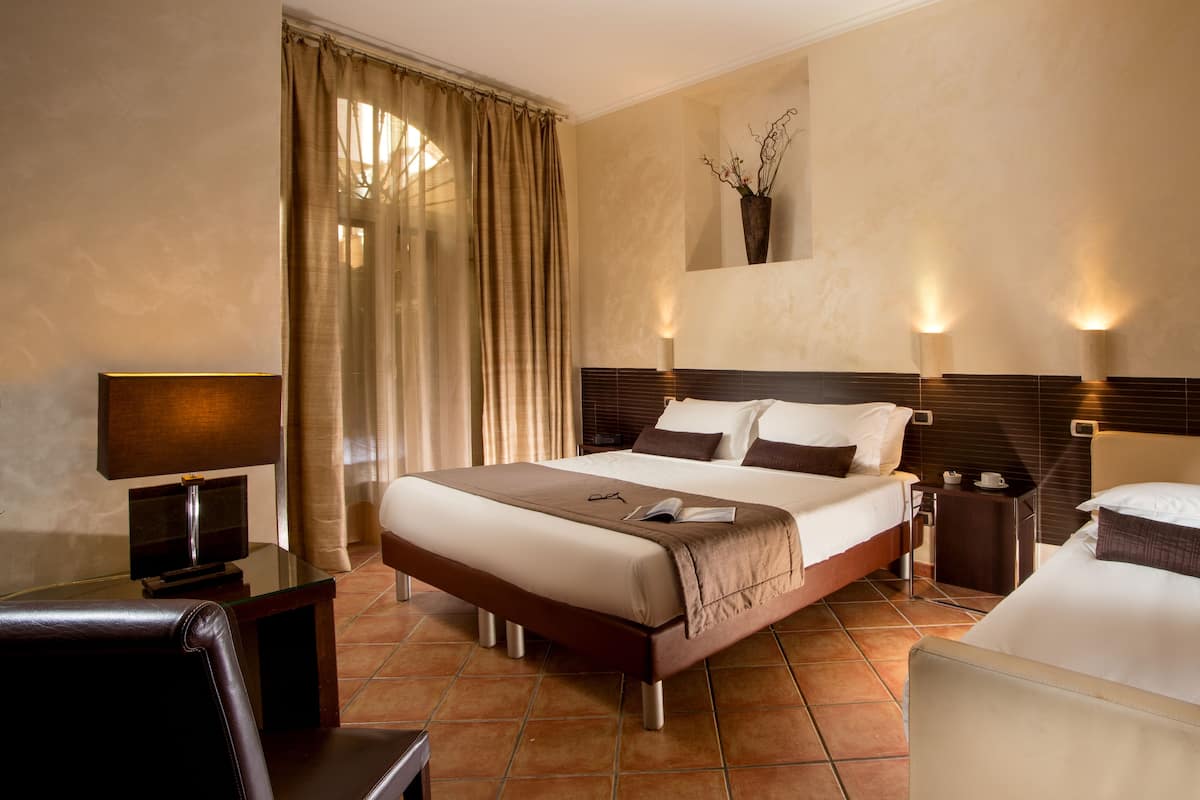 Habitación de hotel con una cama grande, un escritorio con lámpara, una silla y una pequeña mesa con una taza.