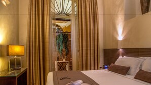 A hotel room with a bed, a bedside table with a lamp, a small table with a bottle and glasses, and a view of a balcony with curtains. - Basilio 55 Rome (Rome)