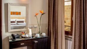 A hotel room with a bed, a bedside table with a phone, a vase with flowers, and a window with curtains. - Basilio 55 Rome (Rome)