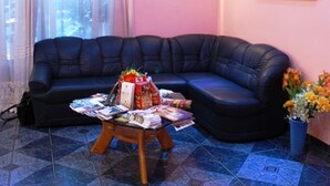Un salón con un sofá de cuero negro, una mesa de centro con libros y un arreglo floral, un cuadro en la pared y una ventana con cortinas de encaje.