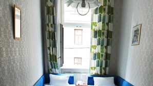 Una habitación pequeña y acogedora con dos camas individuales, una mesa con una lámpara y una ventana con cortinas.