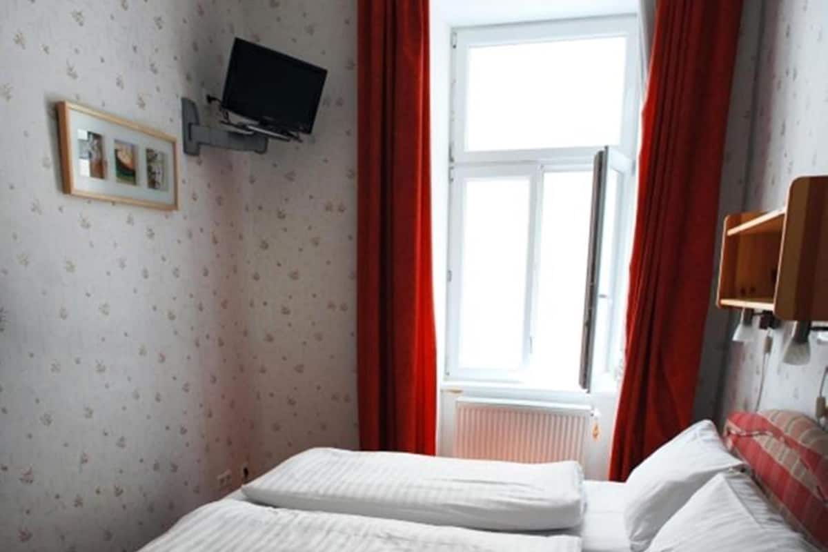 Quarto com cama, televisão na parede e janela com cortinas vermelhas.