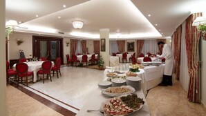 A spacious dining area with multiple tables and chairs, a buffet setup with various dishes, and a waiter attending to guests. - Le Terrazze sul Gargano (San Giovanni Rotondo)