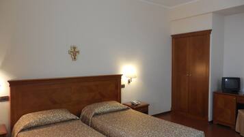 A hotel room with two beds, a wooden wardrobe, a television, and a cross on the wall.