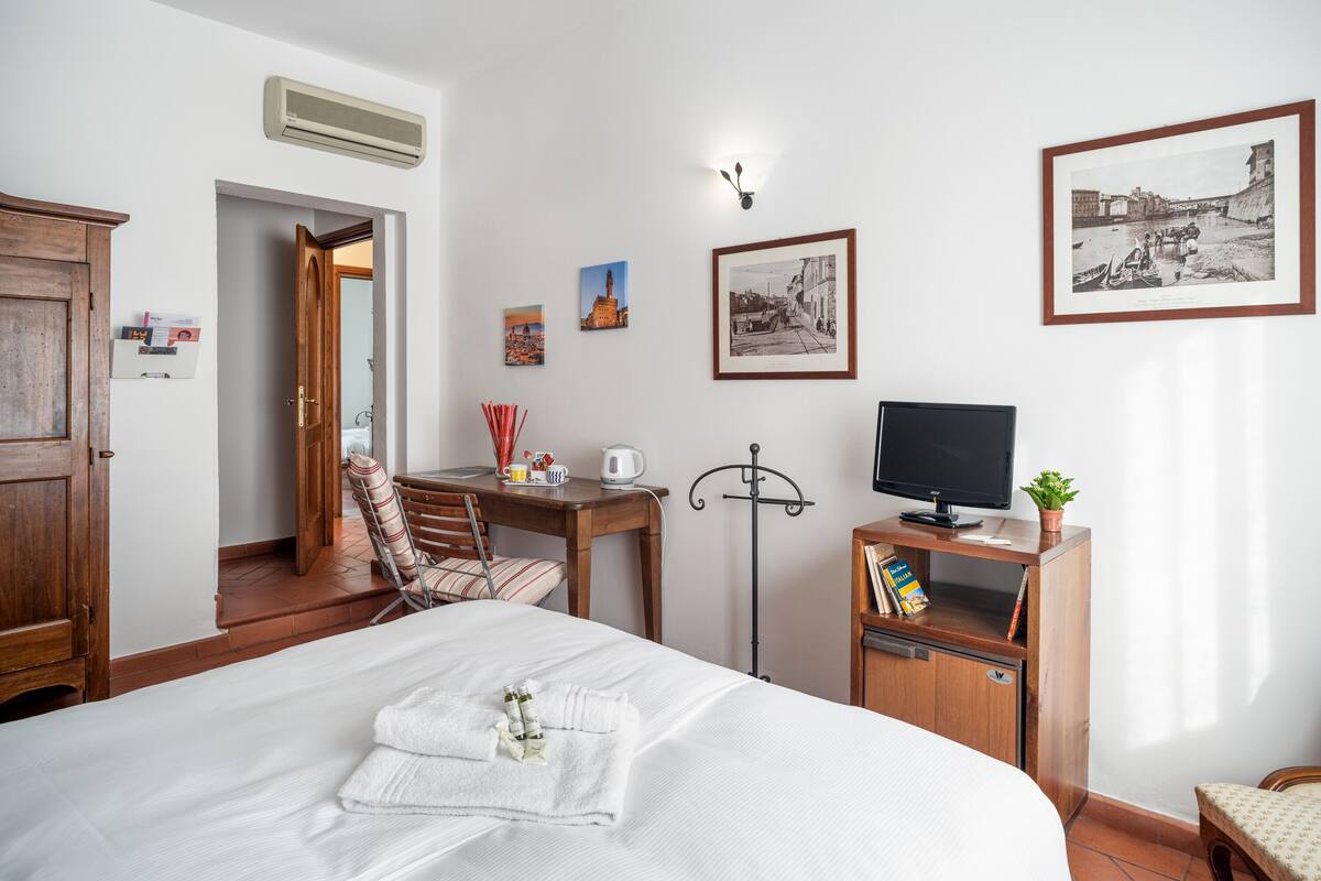 A hotel room with a bed, a desk with a chair, a television, and a bookshelf.