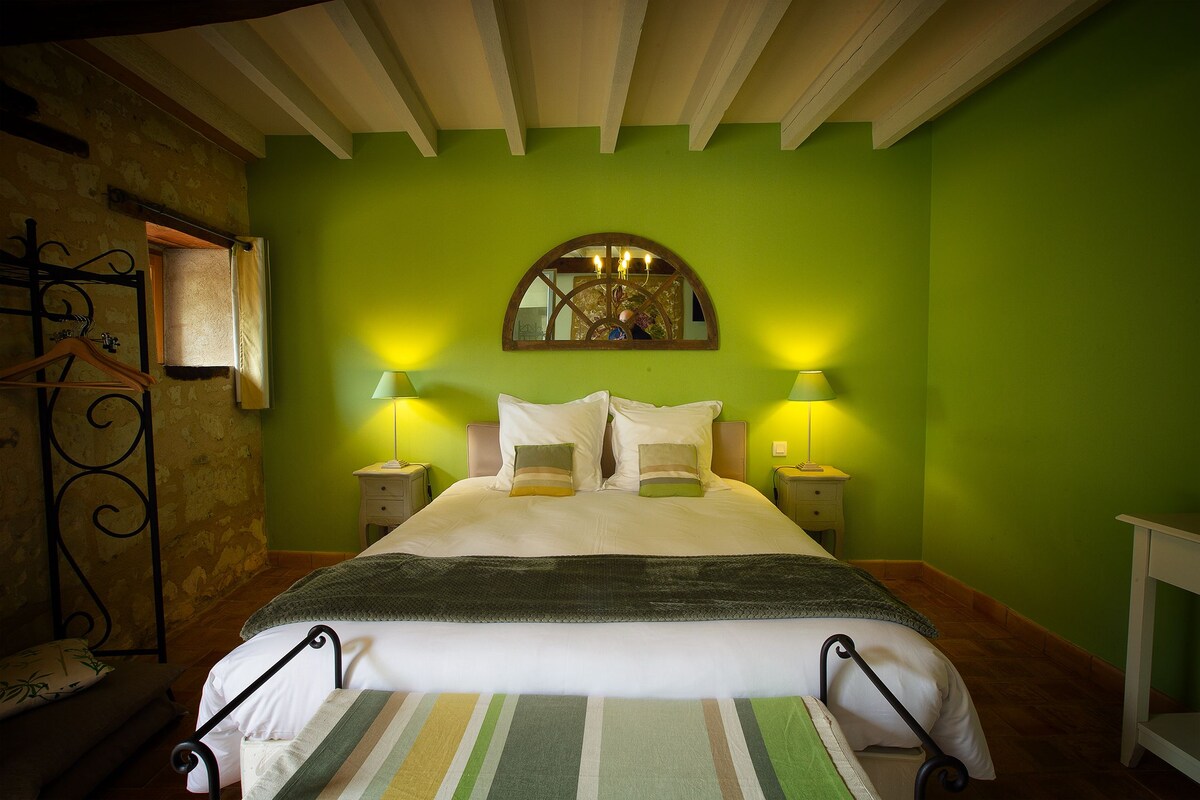 Un dormitorio con una cama grande, paredes verdes, un espejo sobre la cama y dos lámparas de noche.