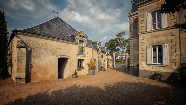 A historic building with a gravel driveway, a covered entrance, and a small garden area. - Le Chai de la Paleine (Le Puy-Notre-Dame)