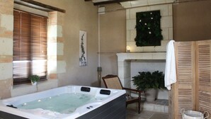A spa room with a hot tub, a fireplace, and a chair. - Le Chai de la Paleine (Le Puy-Notre-Dame)