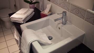 A bathroom with a white sink, a towel rack, a hairdryer, and a potted plant.