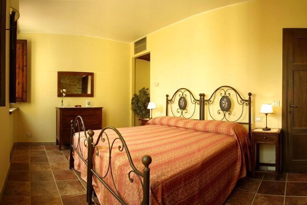 Un dormitorio con cama, mesitas de noche, cómoda, espejo y una puerta.