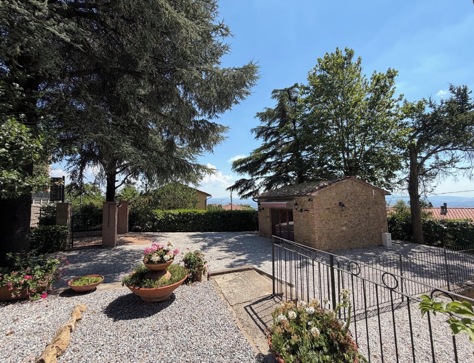 A courtyard with a stone building, gravel ground, and potted plants.
