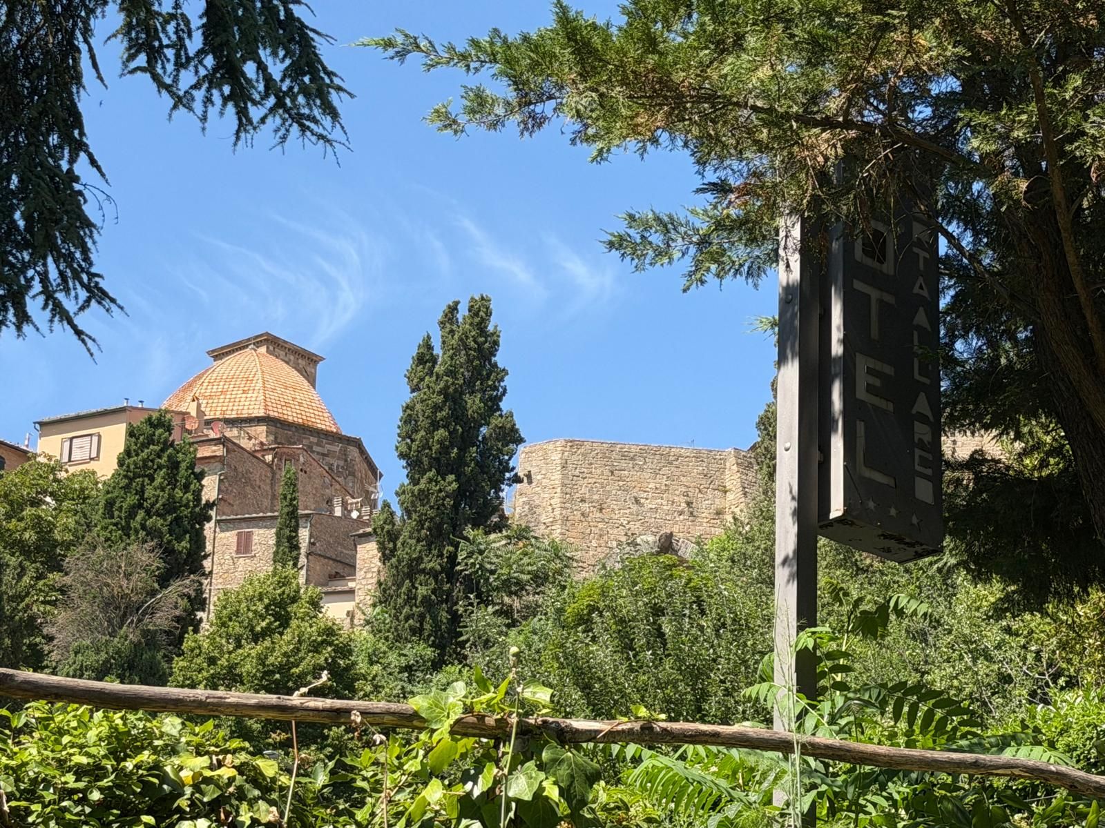 Edificio histórico con pared de piedra y estructura en forma de cúpula, rodeado de vegetación.