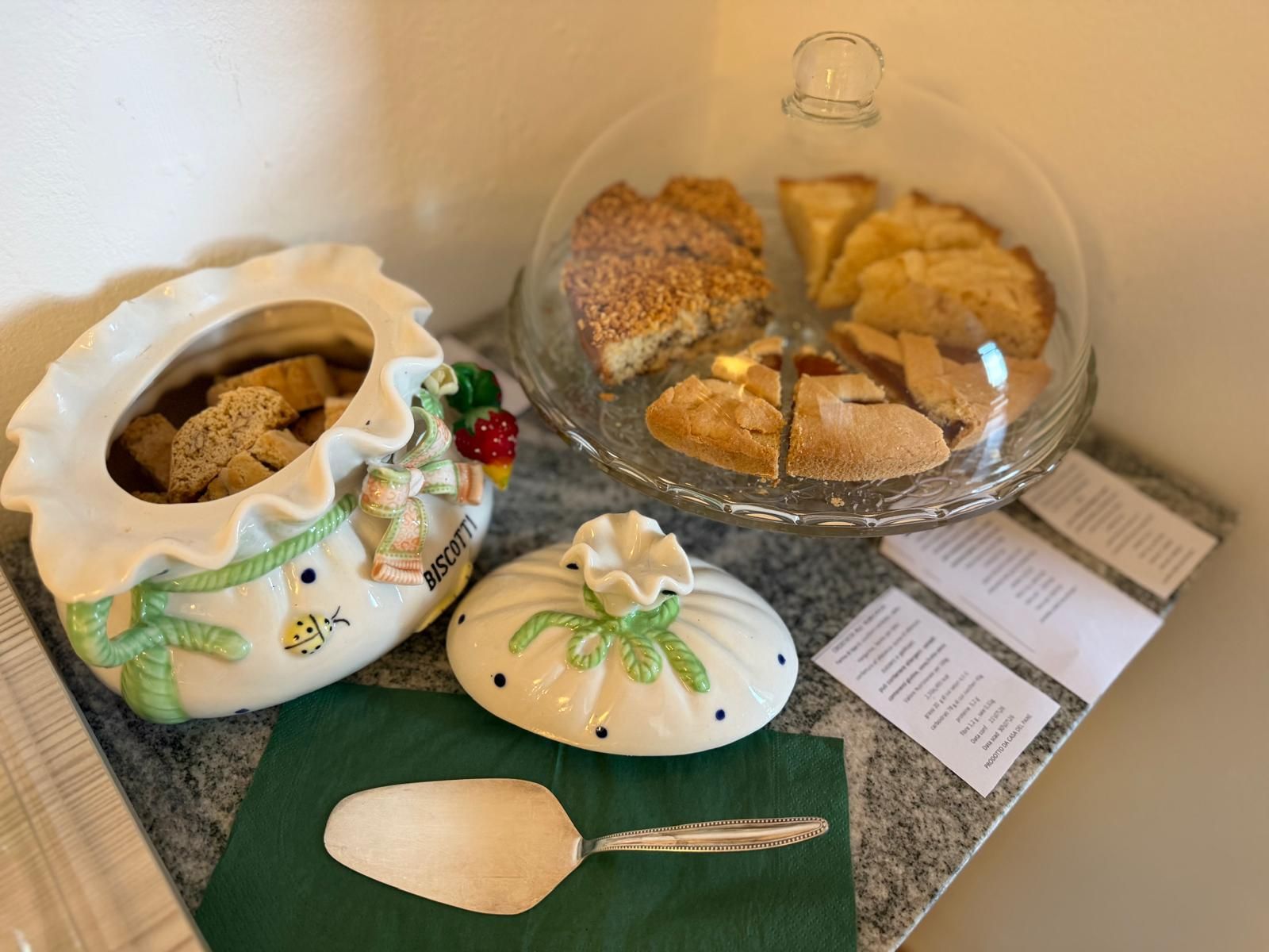 A ceramic dish with a biscuit design, a glass pie dish with a lid, and a spoon on a green napkin.