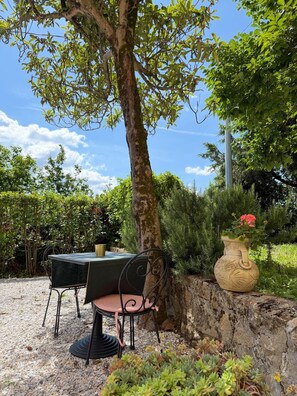 Ein Tisch mit Stuhl im Freien, mit Baum, Steinmauer und Topfpflanze.
