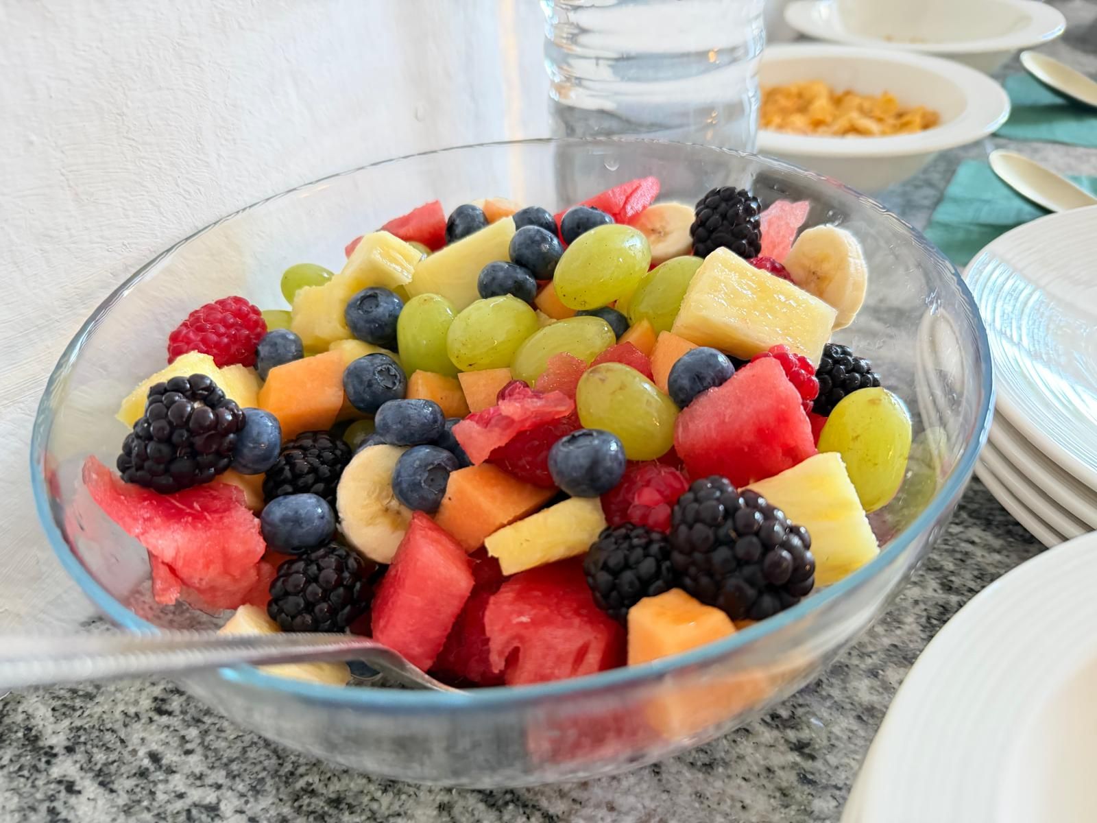 Un cuenco de vidrio transparente lleno de frutas variadas sobre una mesa.