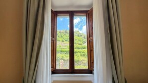 A window with curtains, a view of a green landscape with hills and a stone structure. - Villa Porta all'Arco (Volterra)