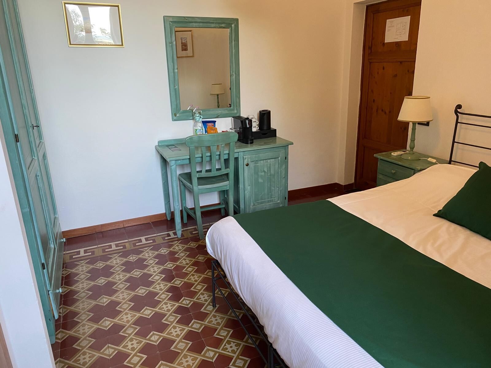 Een slaapkamer met een bed, een bureau met stoel, een kast, een spiegel en een nachtkastje met lamp.