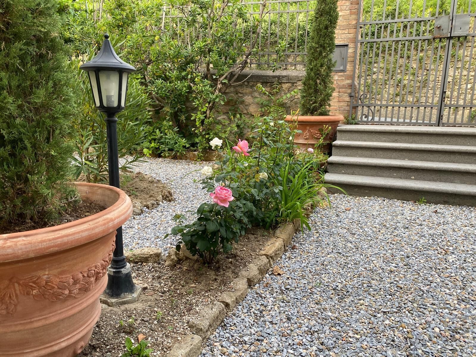 A garden pathway with gravel, potted plants, and a metal gate.