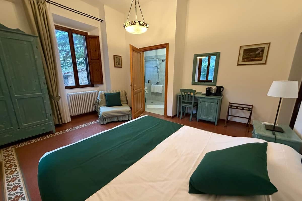 A bedroom with a bed, a desk, a chair, a radiator, a window, and a door.