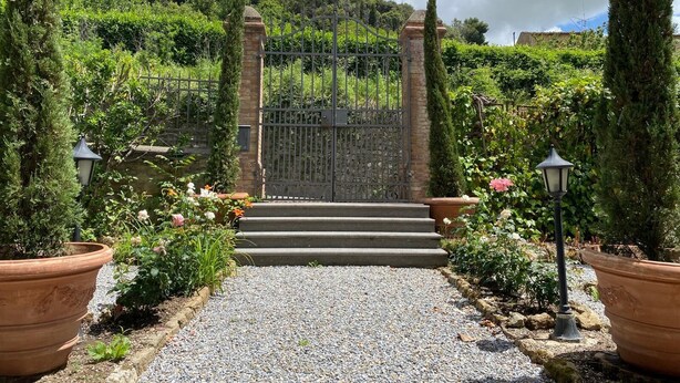 A gated entrance with steps leading up to a gate, surrounded by greenery and potted plants. - Villa Porta all'Arco (Volterra)