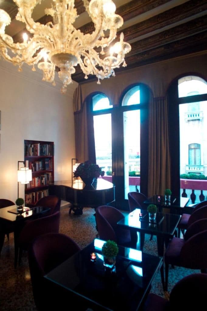 A hotel lobby with a chandelier, bookshelves, and large windows.