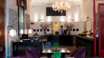 Un hall d’hôtel avec un comptoir d’accueil, un lustre et un grand tableau accroché au mur.