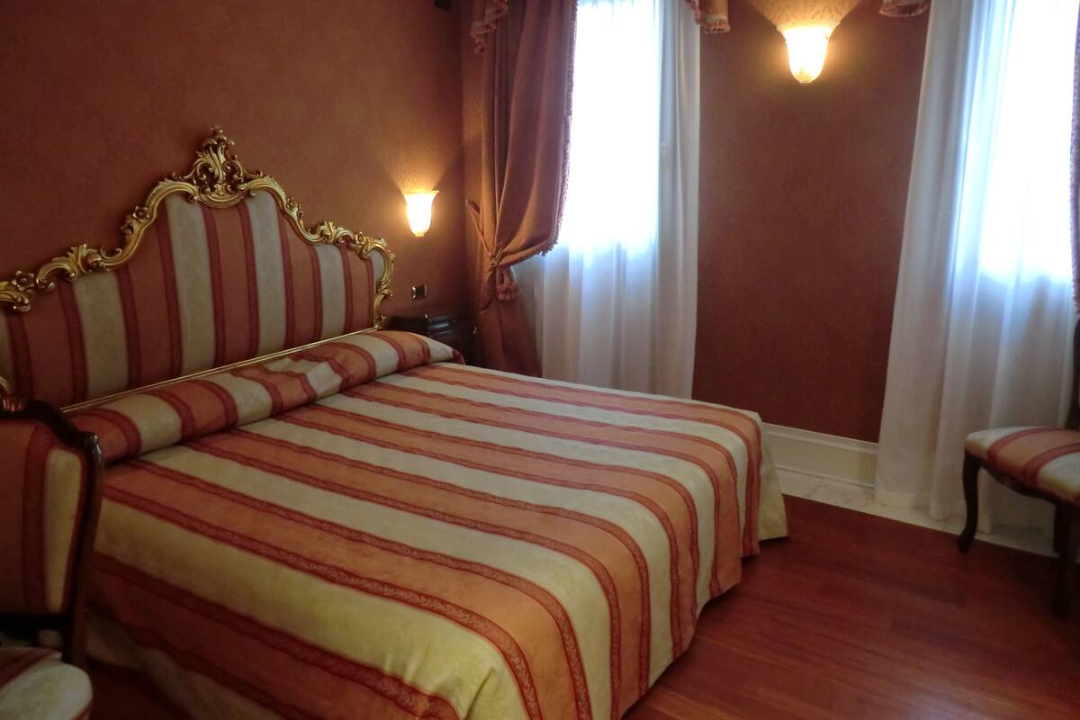 A hotel room with a large bed, a nightstand, and two wall-mounted lamps.