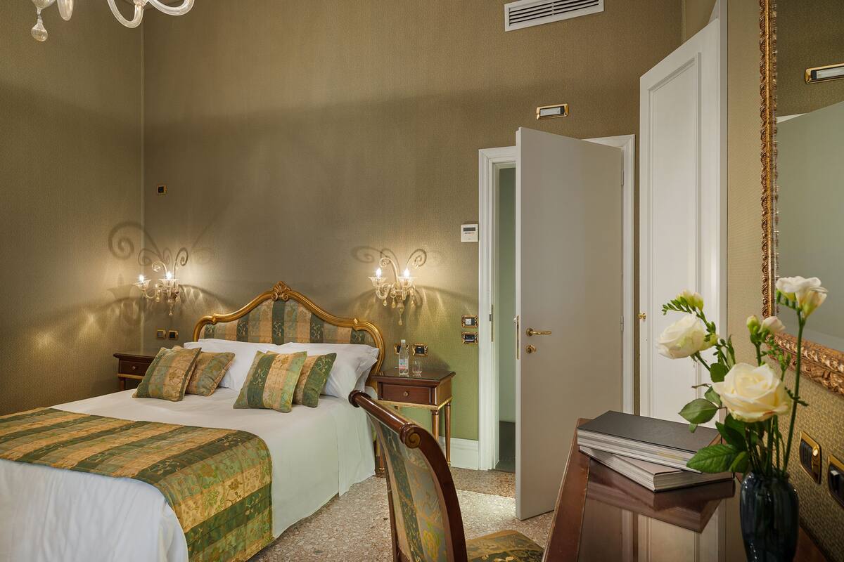 A bedroom with a bed, bedside tables, a mirror, and a vase with flowers.