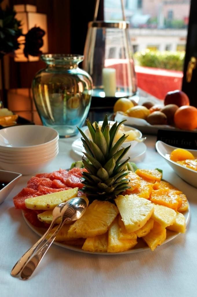 A fruit platter with a pineapple centerpiece, surrounded by various fruits and a candle on a table.