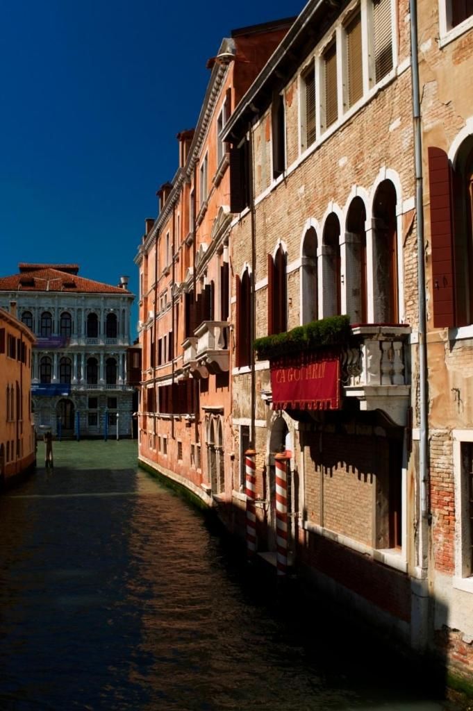 A canal-side building with a red awning, arched windows, and a brick facade.
