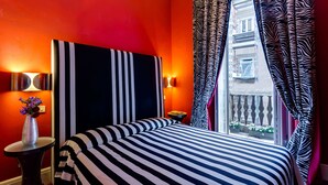Habitación de hotel con una cama a rayas, paredes rojas, cortinas con estampado de cebra y vistas a edificios a través de la ventana.