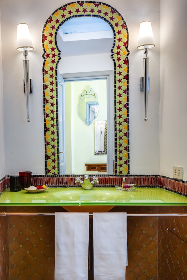 Une salle de bain avec un lavabo vert, deux lampes fixées au mur et un miroir dont le cadre est orné d’un motif en étoile.
