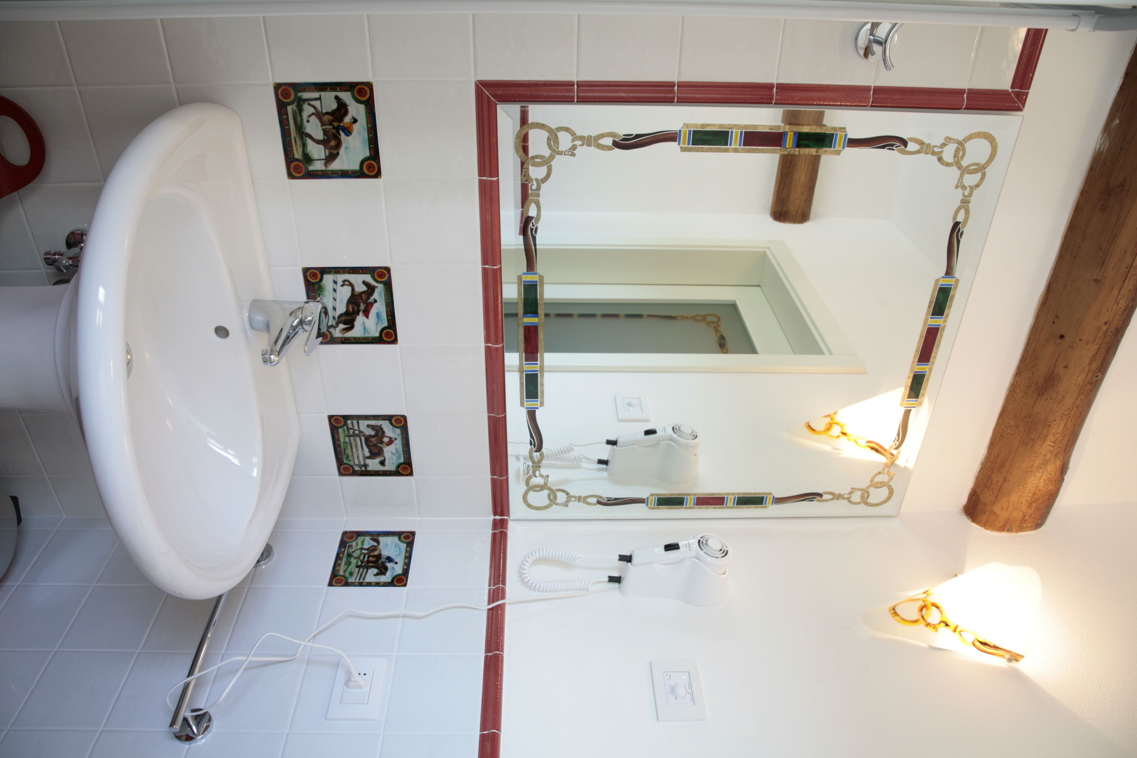 A bathroom with a large white sink, a mirror with a decorative frame, and small decorative tiles on the wall.